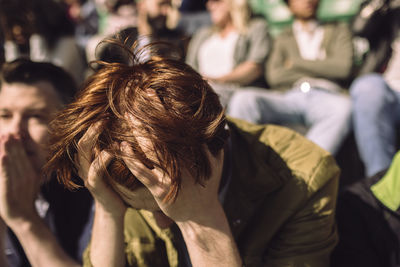Face down young male fan with hand in hair at stadium stand on sunny day