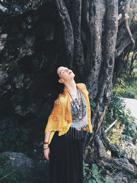 Woman standing by tree trunk in forest