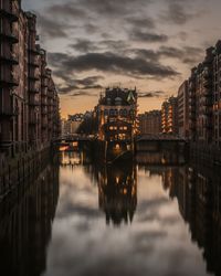 Reflection of illuminated buildings in canal against sky