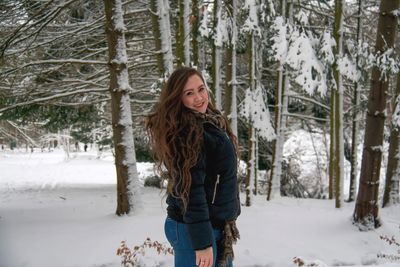 Portrait of smiling young woman standing on snow covered field