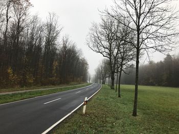 Road amidst bare trees against sky