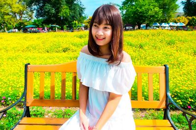 Smiling young woman looking away while sitting on bench against yellow plants