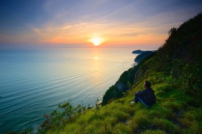 Rear view of woman looking at sea against sky during sunset