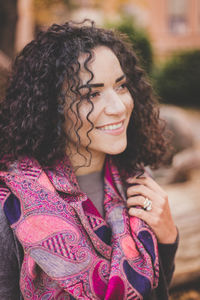 Close-up of smiling woman with curly hair standing outdoors