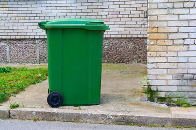 Green garbage can against wall