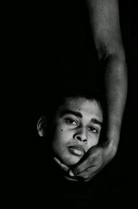 Cropped hand holding head of man against black background