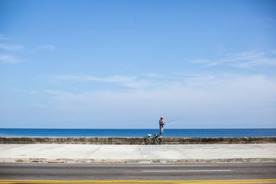 Man sitting on retaining wall fishing in sea