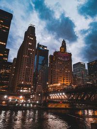 Illuminated buildings by river against sky in city