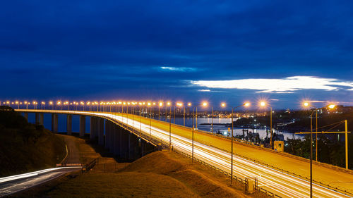 Illuminated bridge over road against sky at night