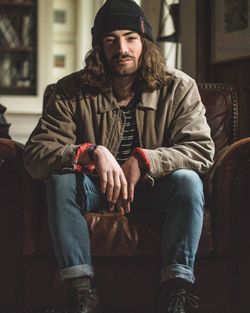 Full length portrait of young man sitting on sofa