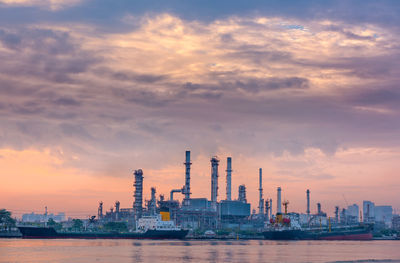 Factory by sea against sky during sunset