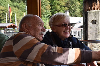 Thoughtful senior couple smiling while sitting against trees