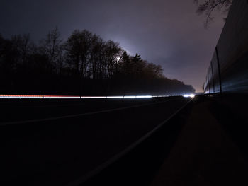 Road by silhouette trees against sky at night