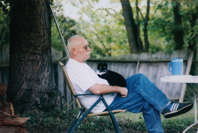 Senior man with cat sitting on chair at yard