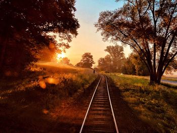 Railroad tracks amidst trees during sunset
