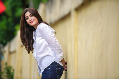 Portrait of young woman standing against wall