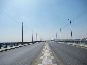 Road by electricity pylon against sky