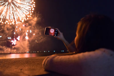 Rear view of woman photographing illuminated mobile phone against sky