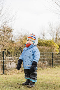 Full length of boy wearing warm clothes while standing on field against sky