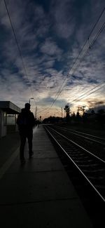 Silhouette people on railroad tracks against sky