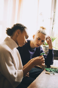 Teenage friends making model together at table by window in room