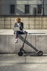 Man using laptop while sitting on retaining wall