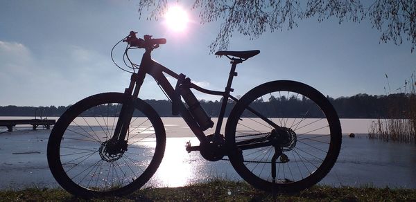 Bicycle by lake against sky during sunset