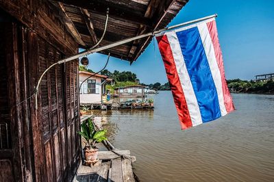 Thai flag on house by river against clear sky