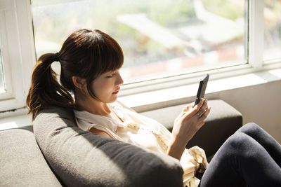 Side view of businesswoman using smart phone on sofa in creative office