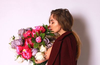 Side view of young woman smelling bouquet against white background