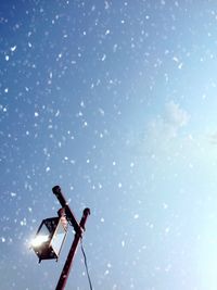 Low angle view of illuminated lighting equipment against sky during snowfall