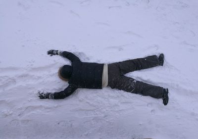 Rear view of man lying on snow covered field