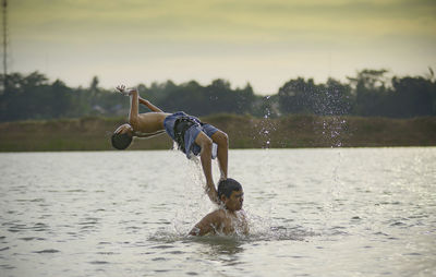 Friends enjoying in lake against sky during sunset