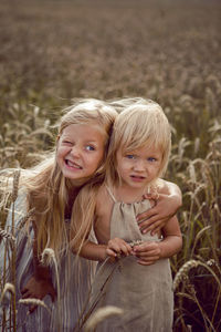 Two sisters blonde girls in dresses stand in a field with wheat ears in the summer