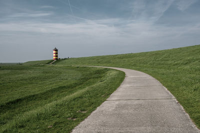 Road leading towards lighthouse amidst field against sky