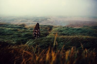 Rear view of woman walking on grassy landscape during foggy weather
