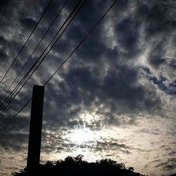 Low angle view of electricity pylon against cloudy sky