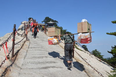 Rear view of man carrying boxes towards people on mount hua