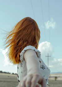 Rear view of young woman standing against sky