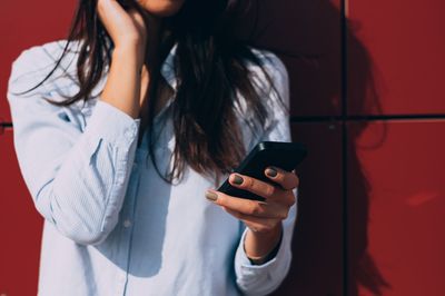 Midsection of woman using mobile phone while standing against wall