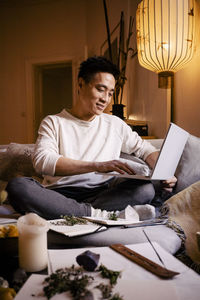 Smiling man using laptop while sitting on sofa in apartment