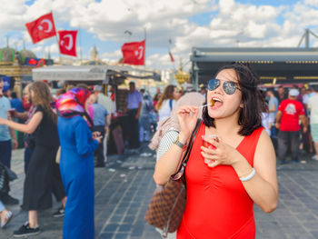 Portrait of woman wearing sunglasses eating pickle while standing in market