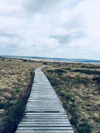 Boardwalk leading towards landscape against sky