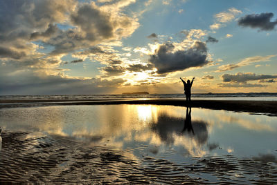 Silhouette person standing in water at sunset