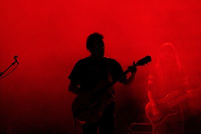 Silhouette man playing guitar against red background