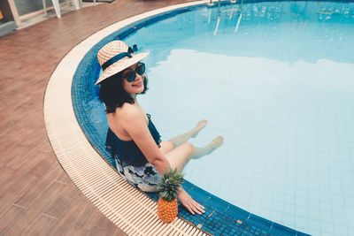 High angle portrait of smiling woman sitting with pineapple at poolside