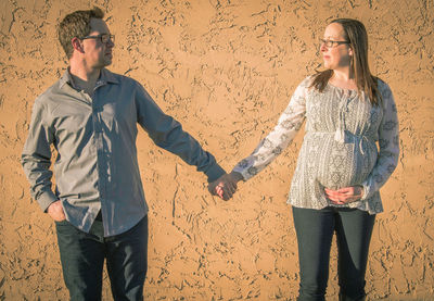 Three quarter length of a young couple standing against wall