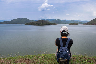 Rear view of man standing by lake against sky