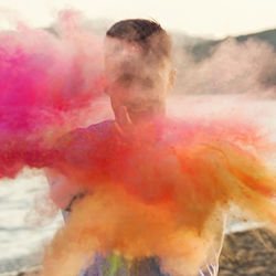 Man playing with powdered paint while standing against sky