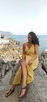 Young woman sitting on rock at beach against sky